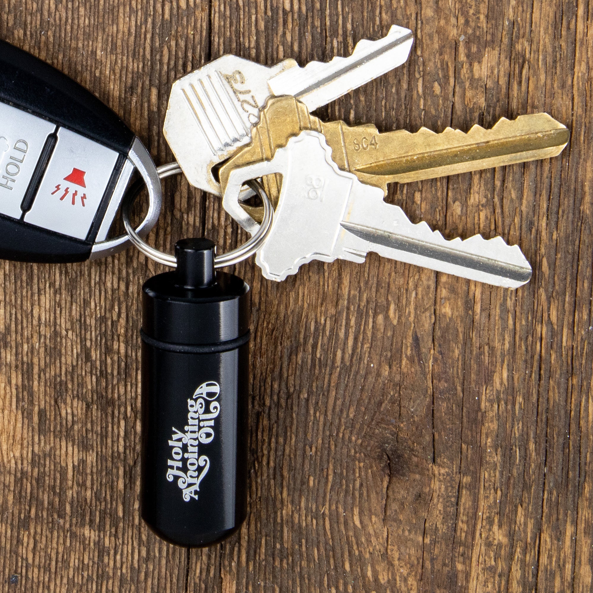Oil Vial Keyring showing keyring vial holder with a set of keys on a wood background