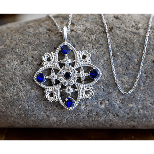 Antique Blue Sapphire September Birthstone Sterling Silver Cross Pendant - With 18" Sterling Silver Chain on a rock