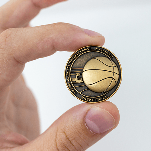Basketball Team Antique Gold Plated Sports Coin in between finger showing the front