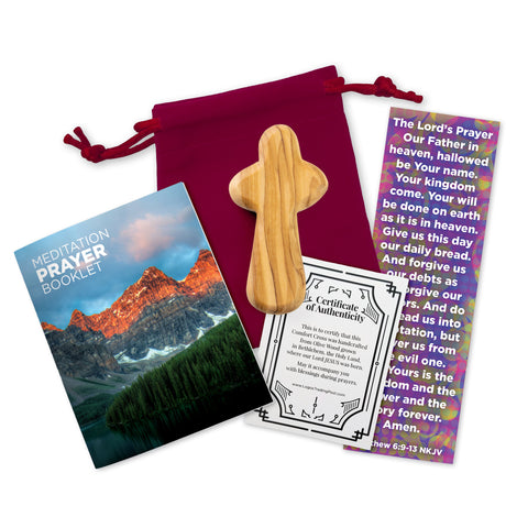 A small olive wood handheld comfort cross, accompanied by a red velvet bag, a 16-page meditation prayer booklet, a Lord's Prayer bookmark and a certificate of authenticity, displayed on a white background.