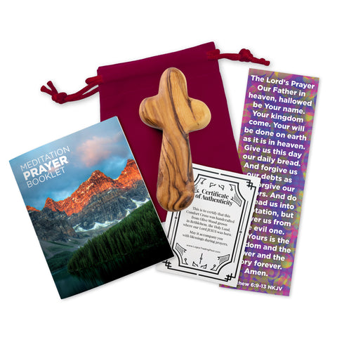 A medium olive wood handheld comfort cross, accompanied by a red velvet bag, a 16-page meditation prayer booklet, a Lord's Prayer bookmark and a certificate of authenticity, displayed on a white background.
