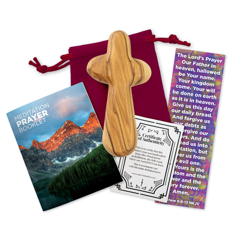 A large olive wood handheld comfort cross, accompanied by a red velvet bag, a 16-page meditation prayer booklet, a Lord's Prayer bookmark and a certificate of authenticity, displayed on a white background.