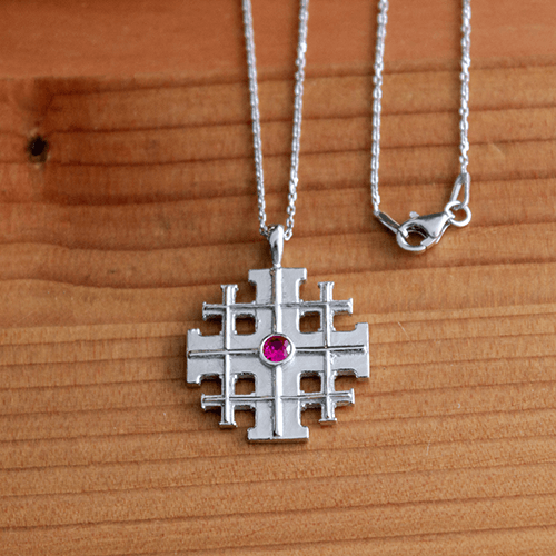 Jerusalem Cross with CZ Ruby, Sterling Silver Pendant - 18 Inch Chain on a wooden table