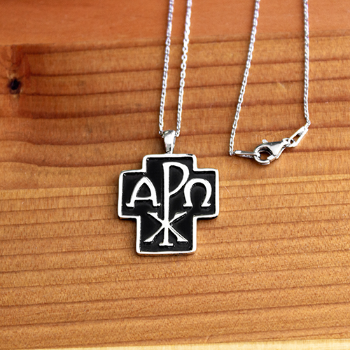 Alpha and Omega Cross Sterling Silver Pendant - 18 Inch Chain on a wooden table